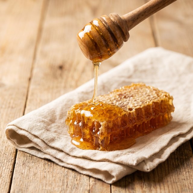 Golden honey drizzling from a wooden dipper into a small jar.